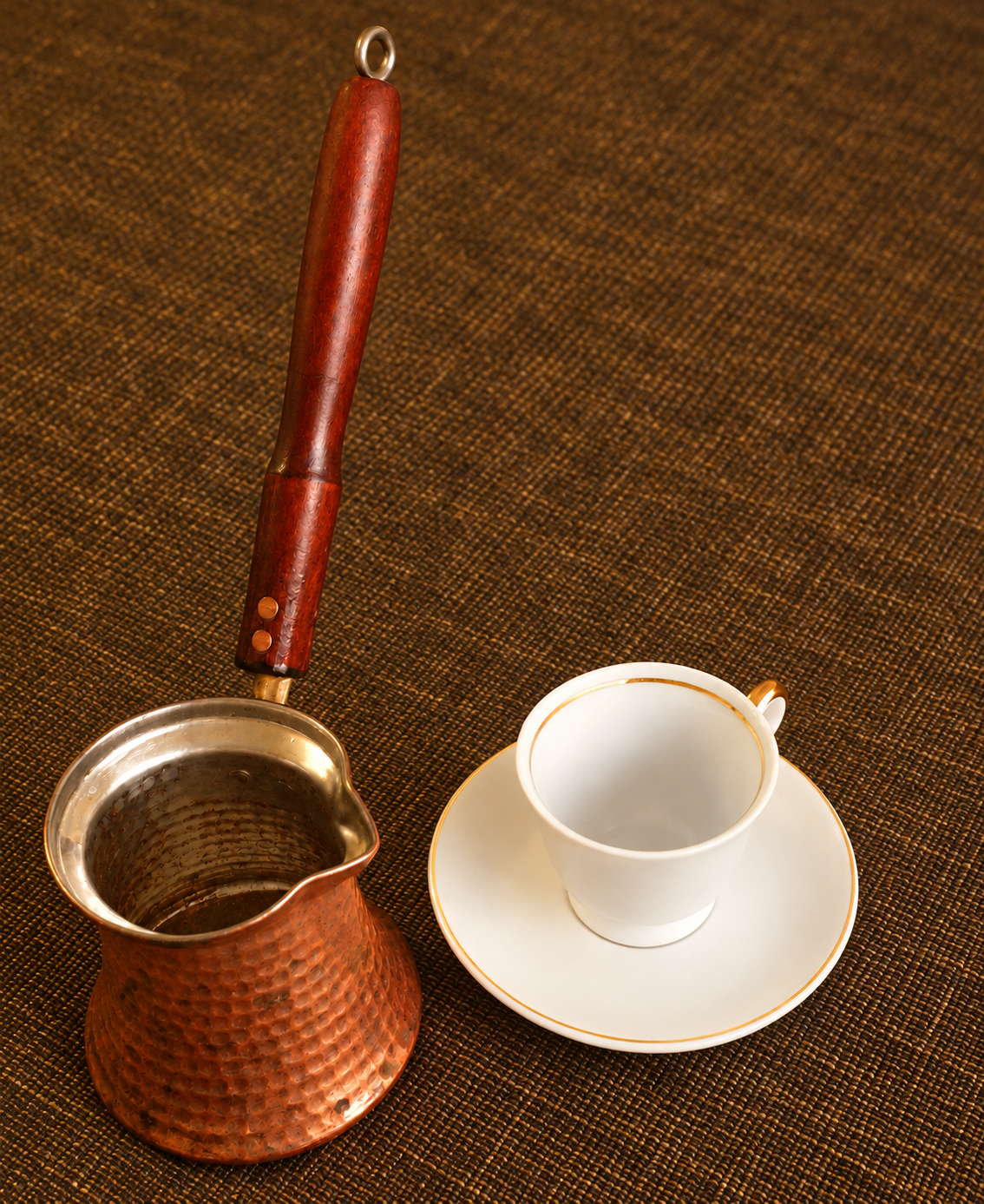 Kupferkanne und weisse Kaffeetasse auf braun-goldenem Stoff